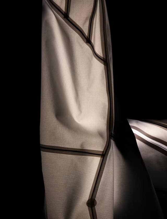 Translucent white fabric with dark geometric seams against a black background.