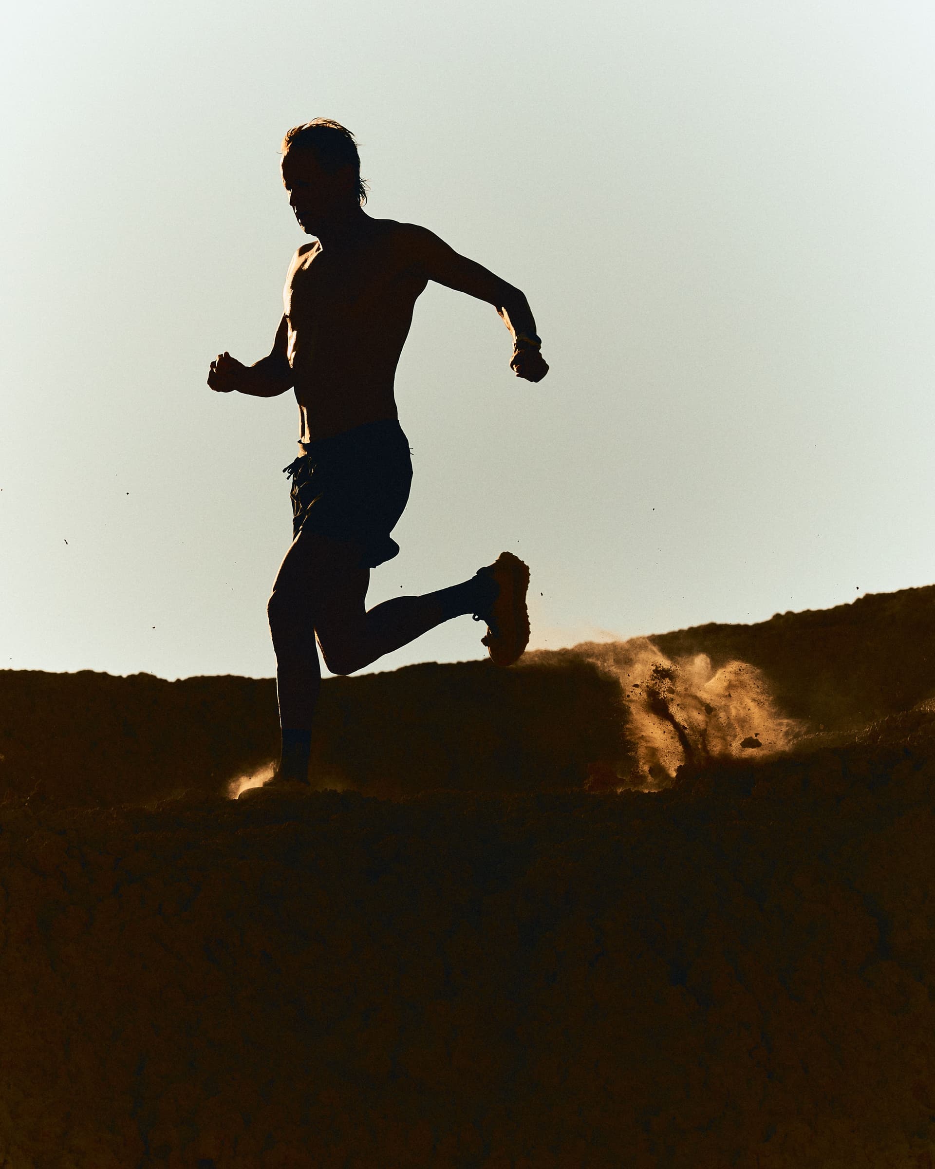 Silhouetted runner on a dirt path, kicking up dust.