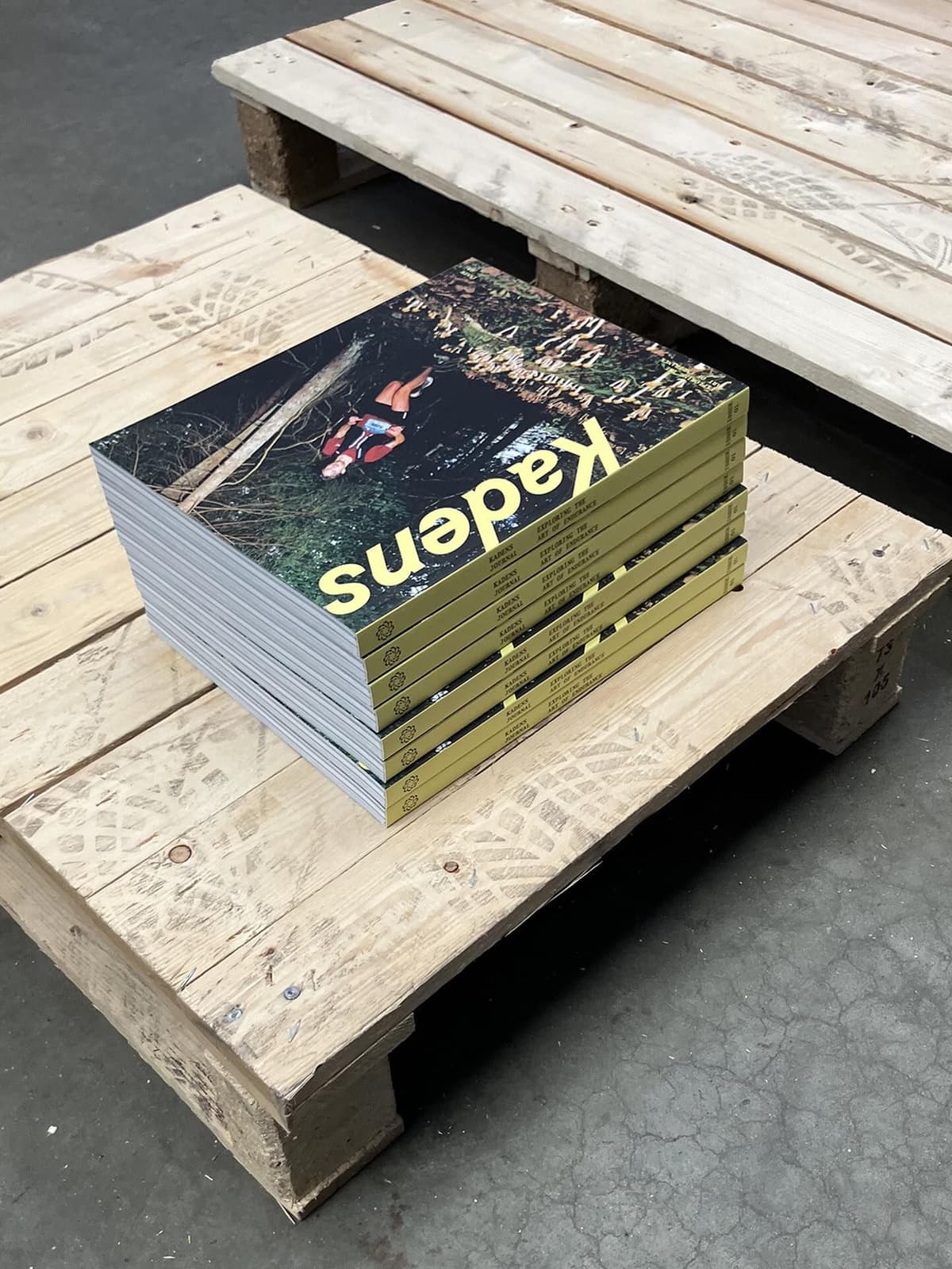 A stack of "Kadens" magazines with yellow spines and a cover image of a person in water, resting on a wooden pallet.