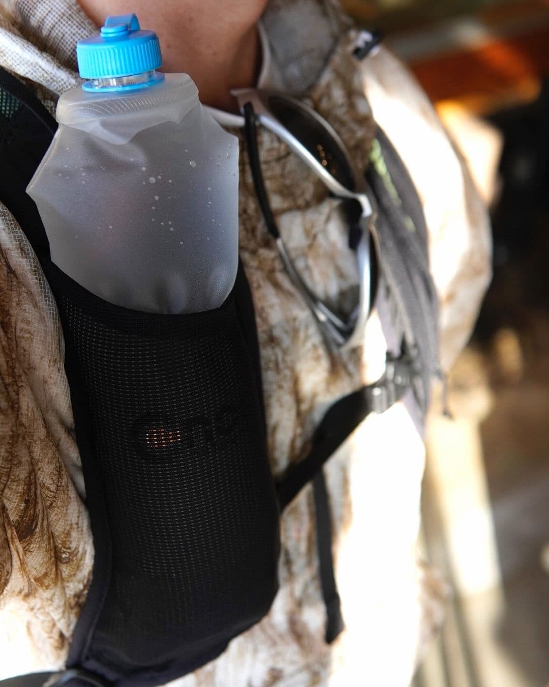 Soft water bottle in a vest pocket, with sunglasses on a shirt collar.
