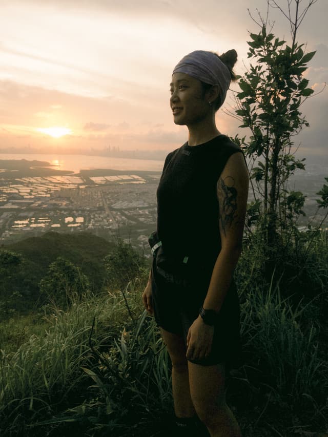 A woman on a mountain at sunset, overlooking a city and bay.