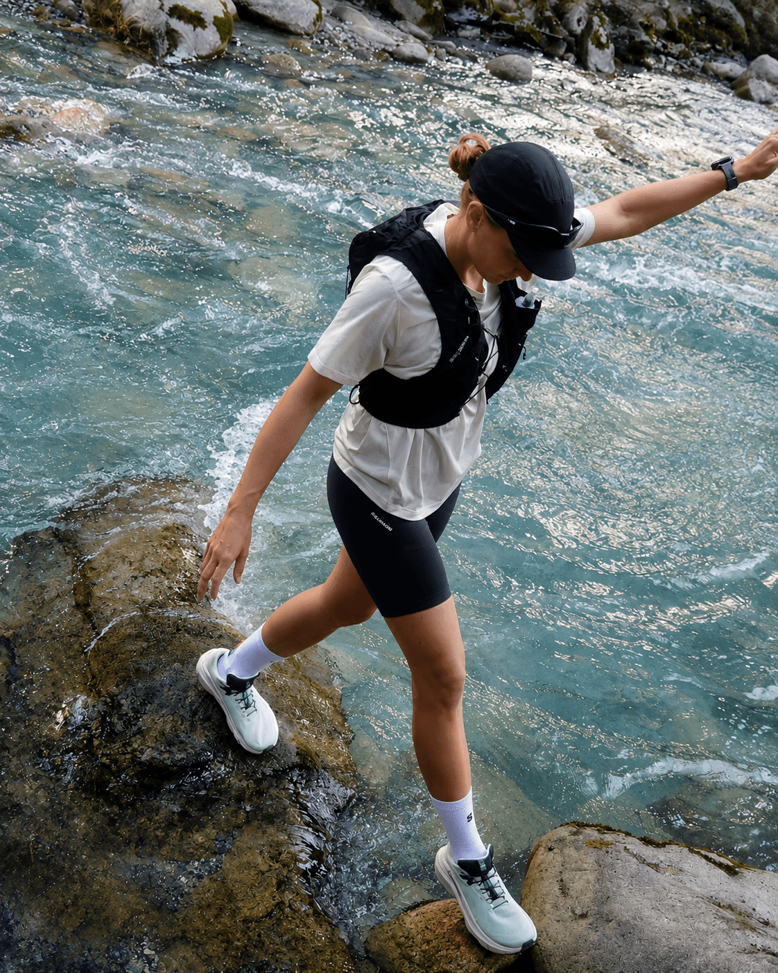 A black mesh hydration vest with two lime green soft flasks lies on dry, cracked earth.