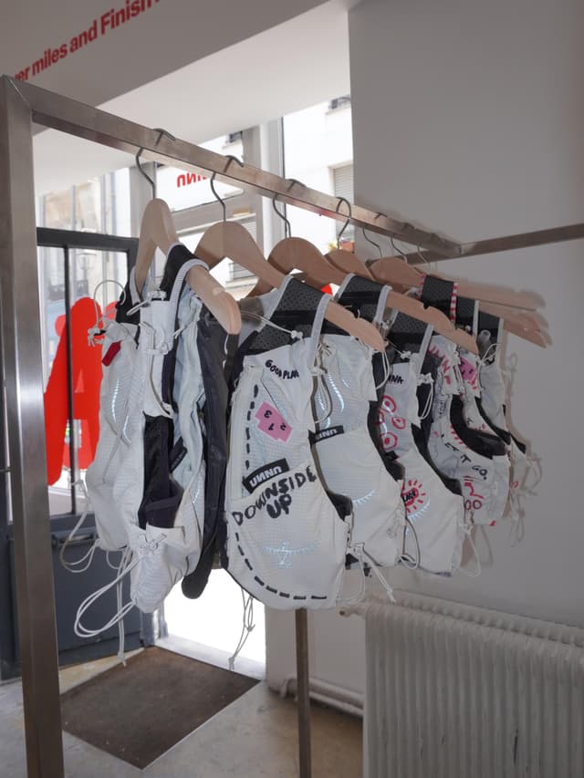 White and black running packs with graphic designs hang on a metal clothing rack in a bright store.