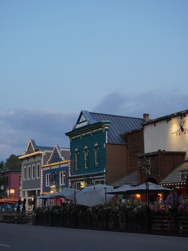 A row of historic-style buildings with outdoor patios and string lights at dusk.