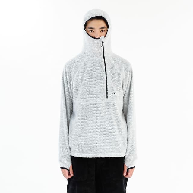 A person wearing a light grey fleece hooded pullover with a black half-zip and mountain logo.