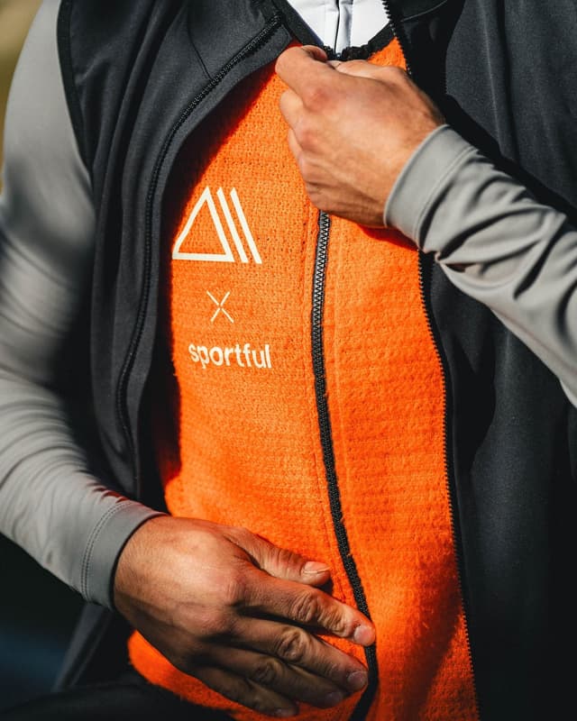 A person zipping up an orange fleece mid-layer with white Sportful logo.