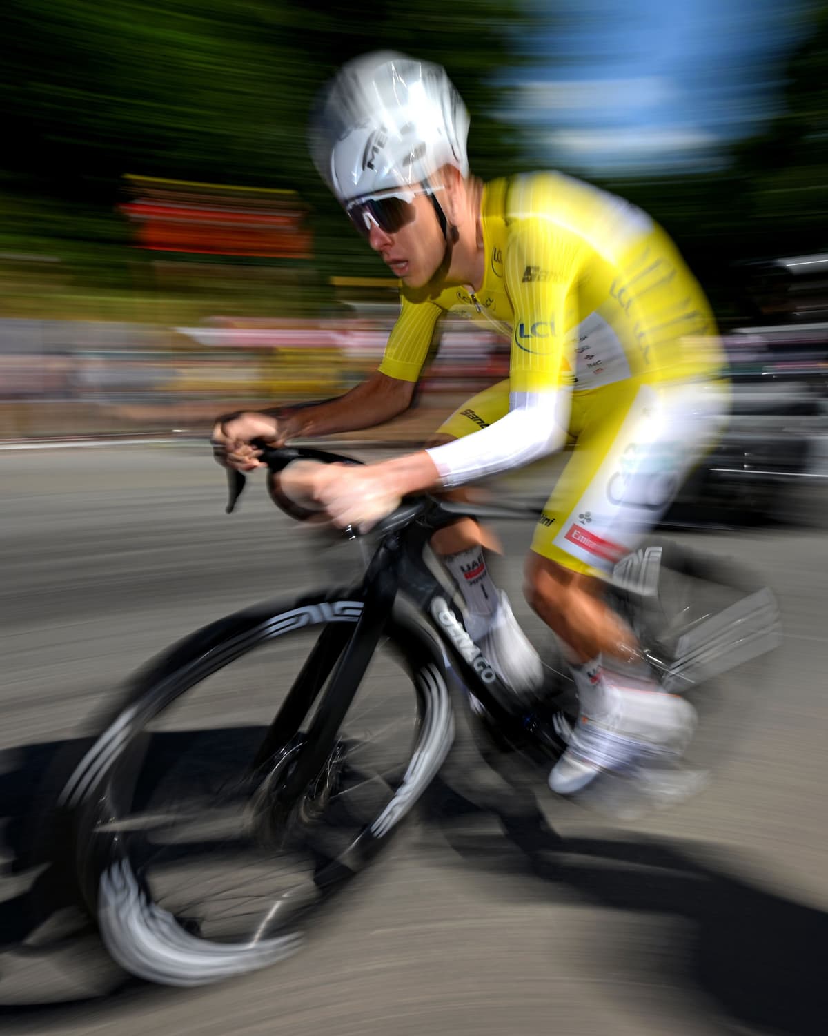 A cyclist in a yellow kit and grey helmet speeds on a black racing bike, captured with motion blur.
