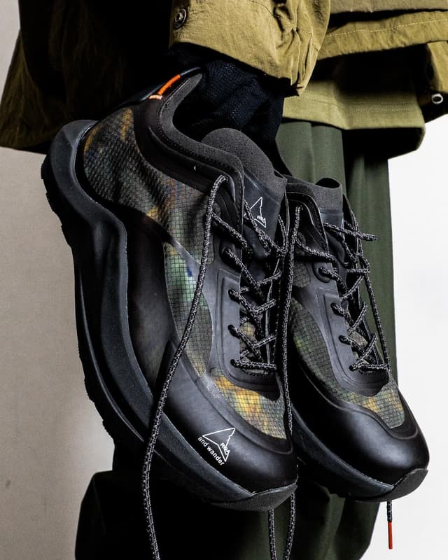 Two black and camouflage-patterned trail shoes with mesh overlays and thick laces, held up.