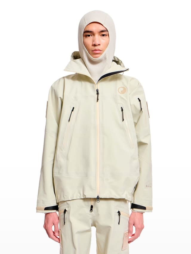 A man wearing a light beige balaclava and matching technical jacket and pants.