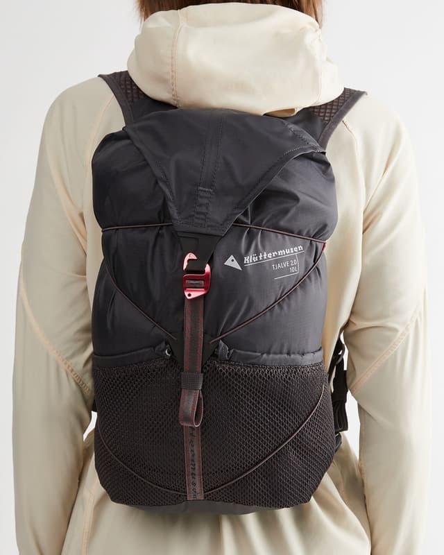 Black Klättermusen Tjálve 2.0 10L backpack with a red buckle and mesh pockets, worn on a person's back.