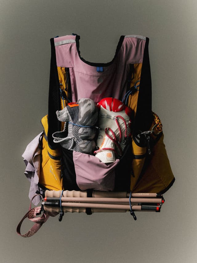 A pink, yellow, and black trail running vest packed with shoes, a red helmet, and trekking poles.