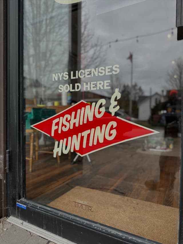 Glass door with signs reading "NYS LICENSES SOLD HERE" and "FISHING & HUNTING".
