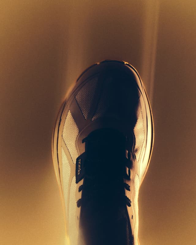 Top-down view of a dark running shoe with mesh, laces, and a small 'norba' tag, glowing against a warm orange background.