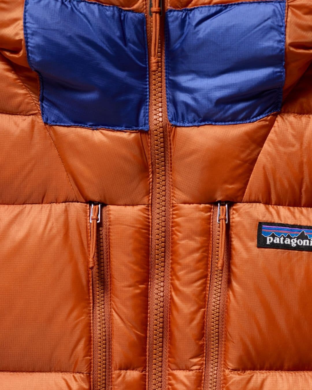 Orange puffer jacket with blue panels, a main zipper, and a Patagonia logo.