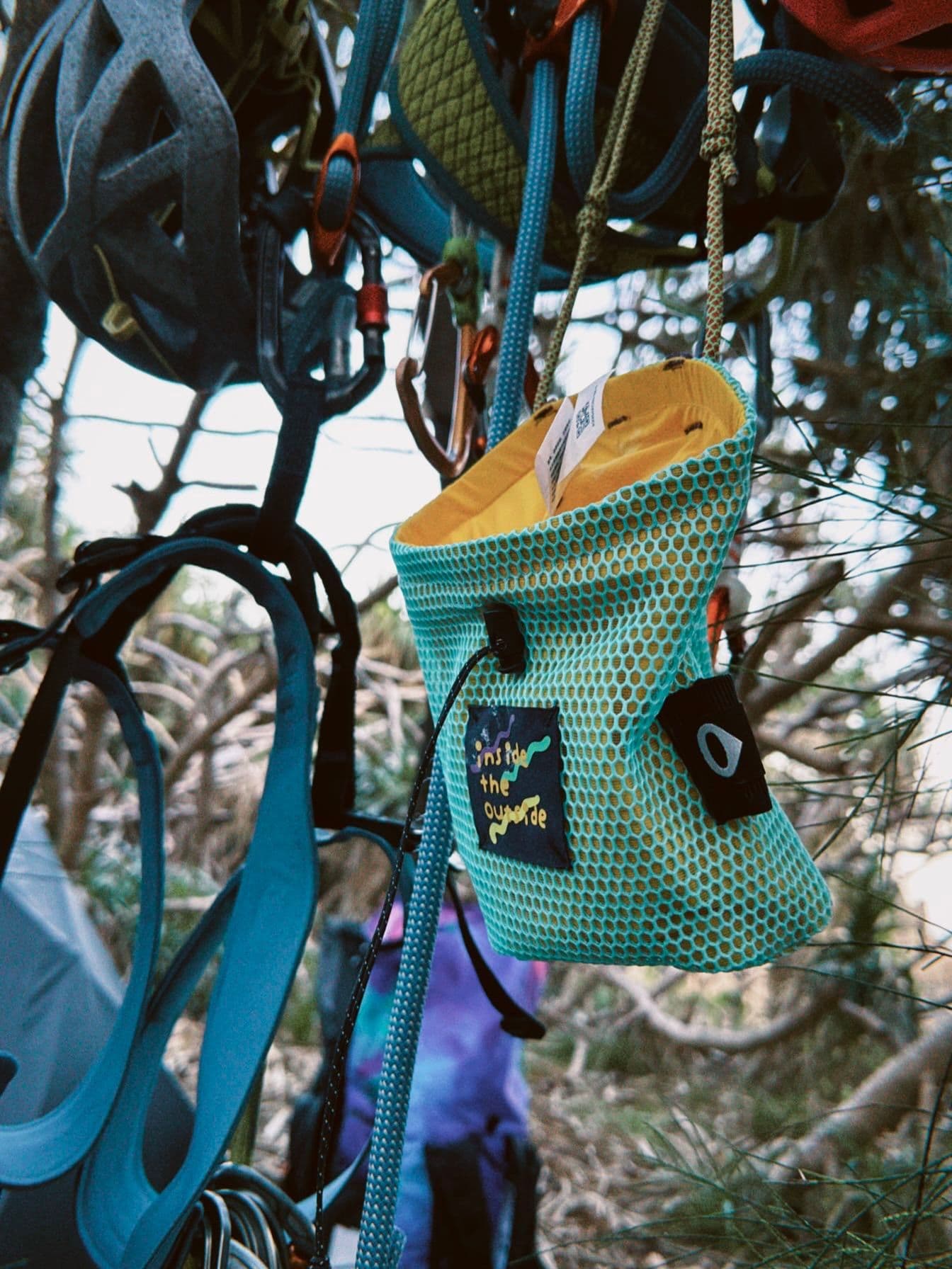 Climbing gear, including a helmet and a teal mesh bag, hangs from ropes in a natural outdoor setting.