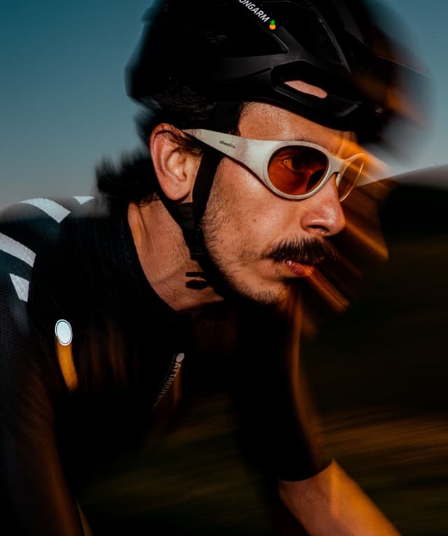 Close-up of a male cyclist in a helmet and orange-tinted glasses, blurred by motion at dusk.