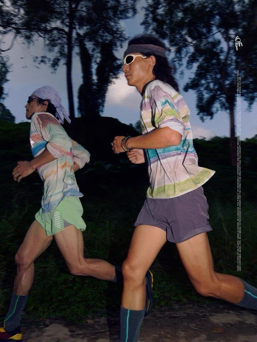 Two people run outdoors on a trail, wearing colorful athletic gear and sunglasses.