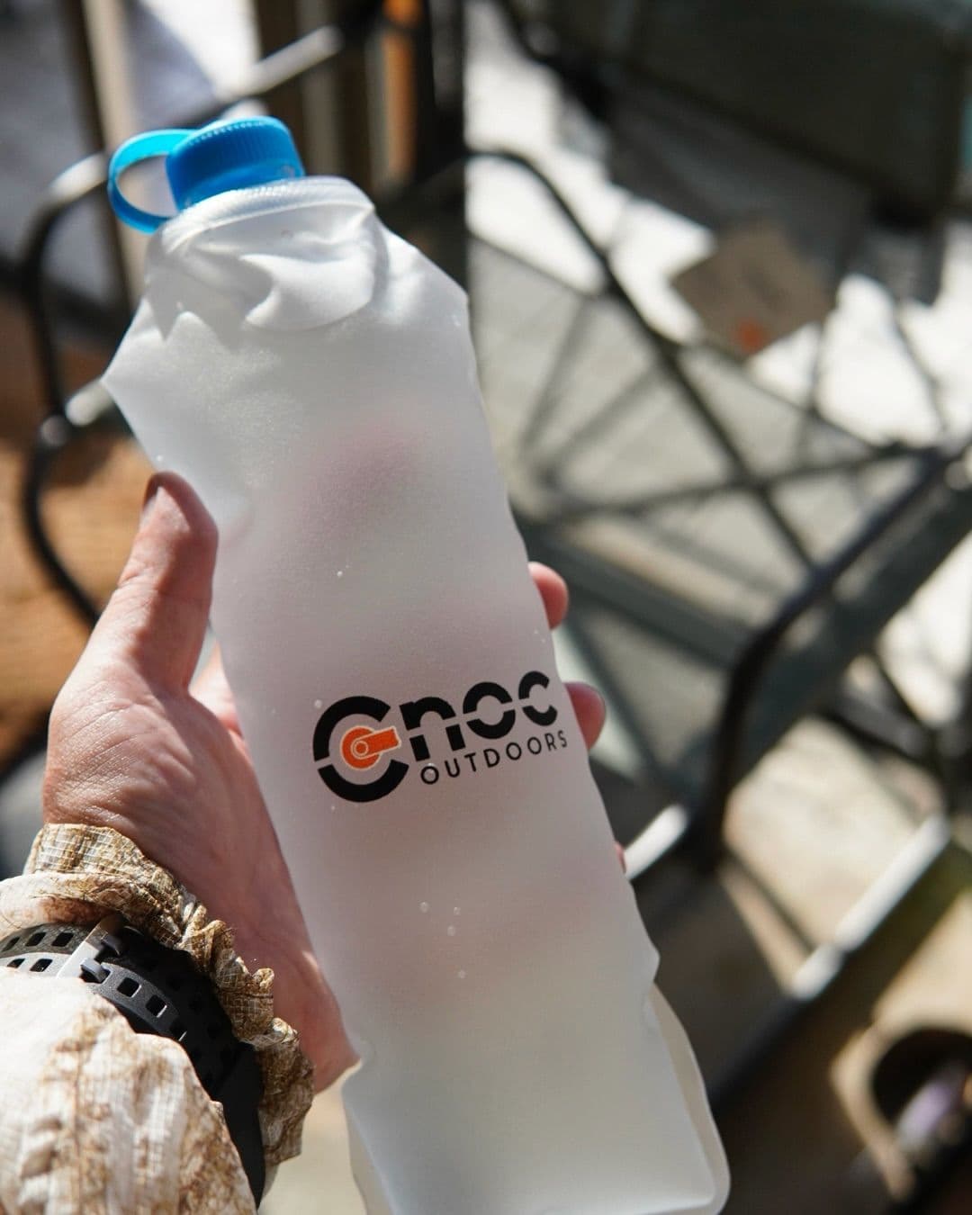 Hand holding a frosted CNOC OUTDOORS flexible water bottle with a blue cap and condensation.