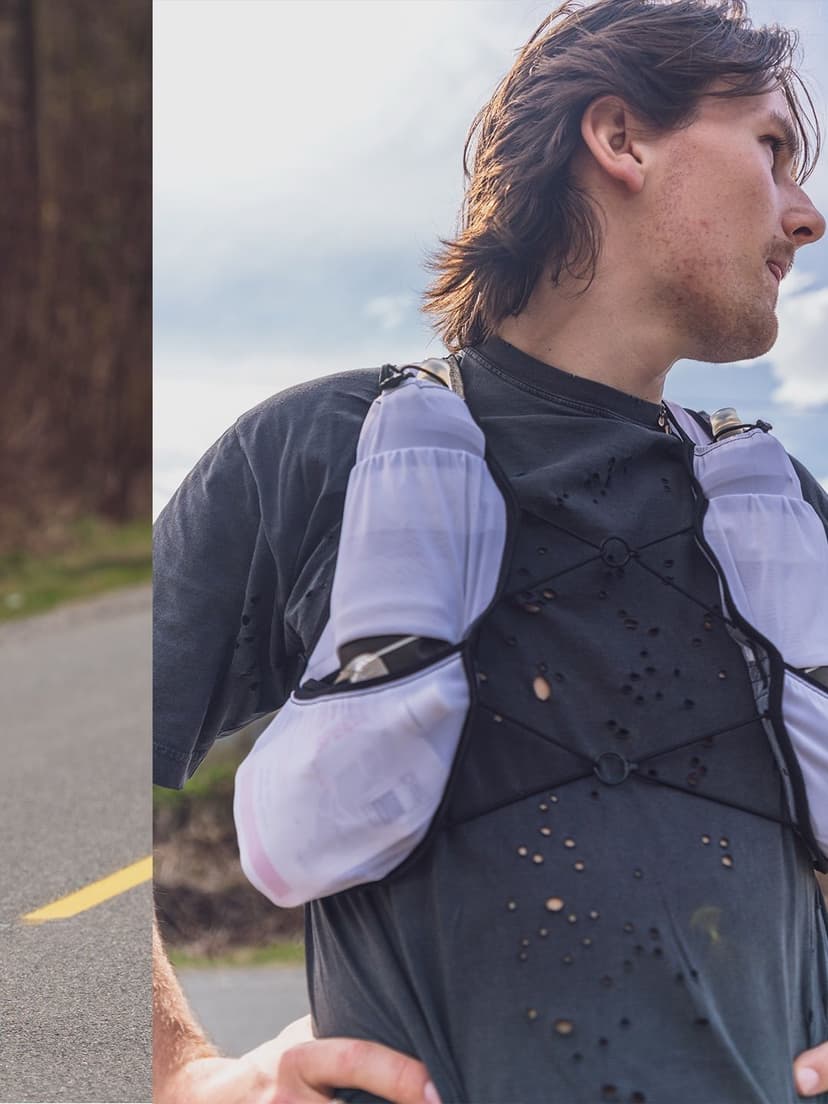 Man wearing a running vest with water bottles on a road.