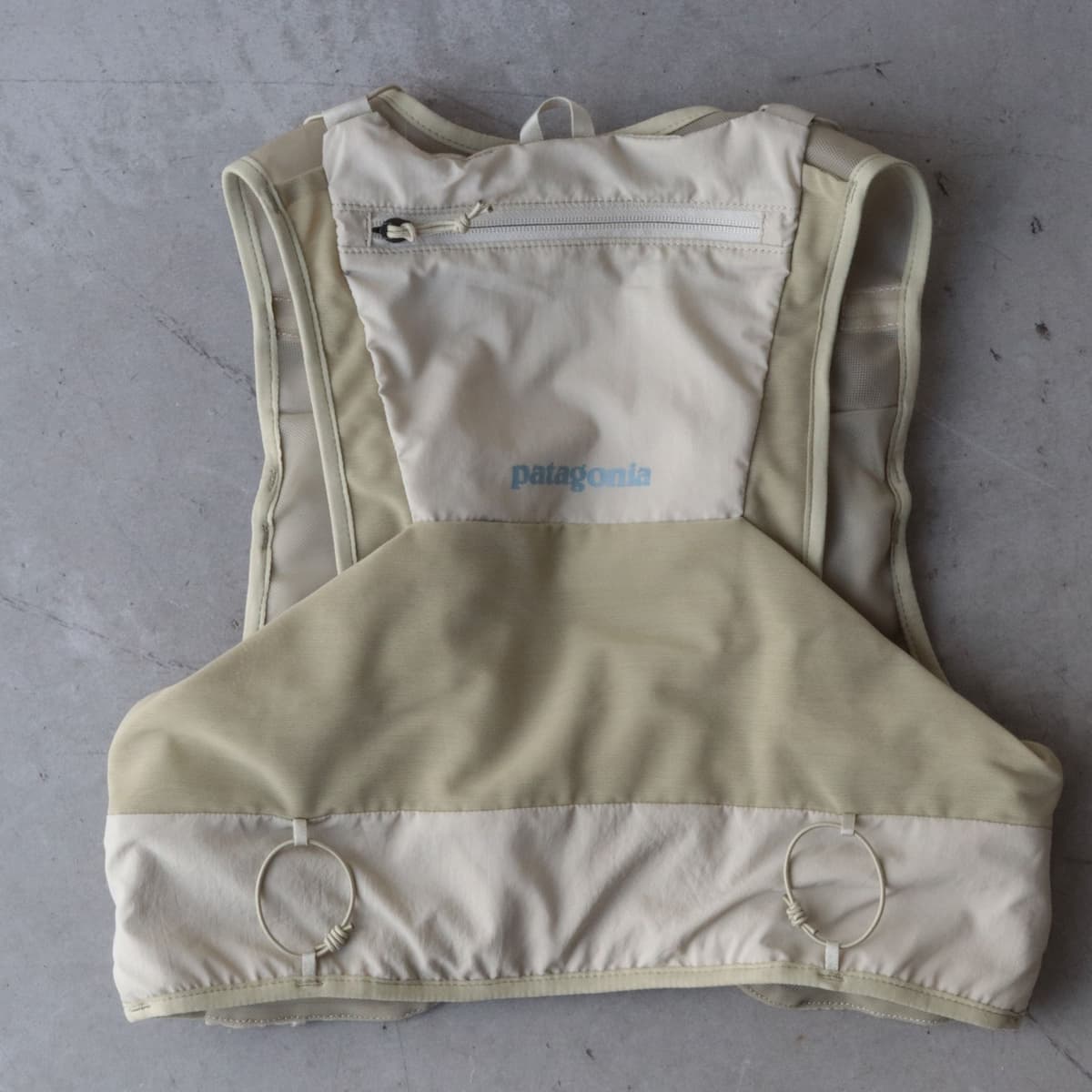 Light beige Patagonia fly-fishing vest, back view, with a zippered pocket.