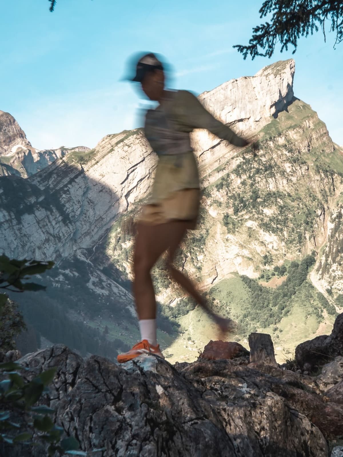 Motion-blurred person trail running on a rocky cliff edge with a mountain range and valley in the background.