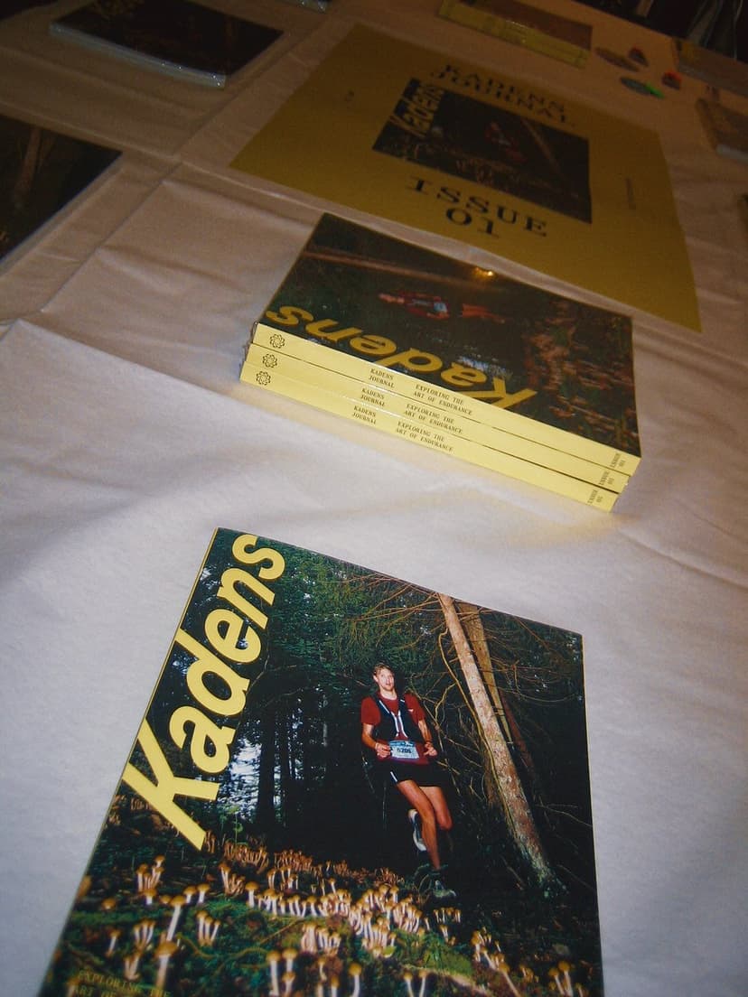 Copies of Kadens journal displayed on a table, including one with a runner in a forest on the cover.