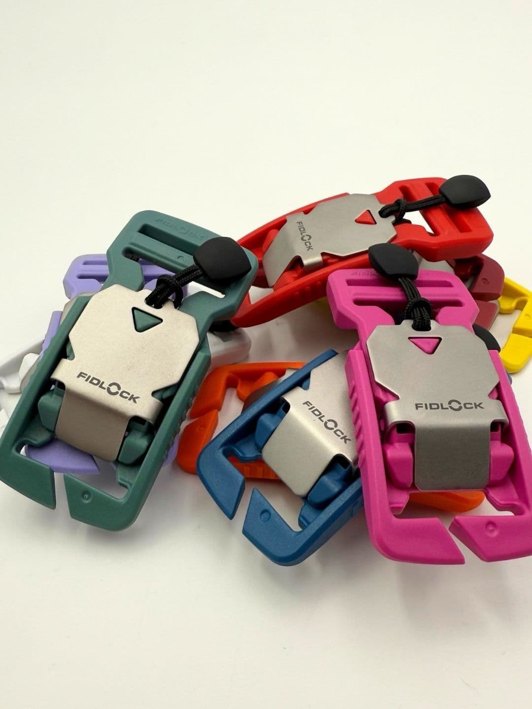 A pile of colorful Fidlock magnetic buckles in various colors, including green, pink, red, and blue.