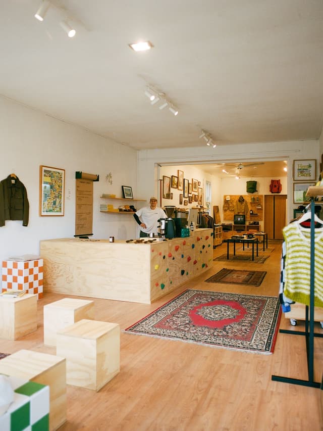 A person stands behind a light wood counter adorned with colorful climbing holds in a bright, modern store with wooden floors and merchandise.