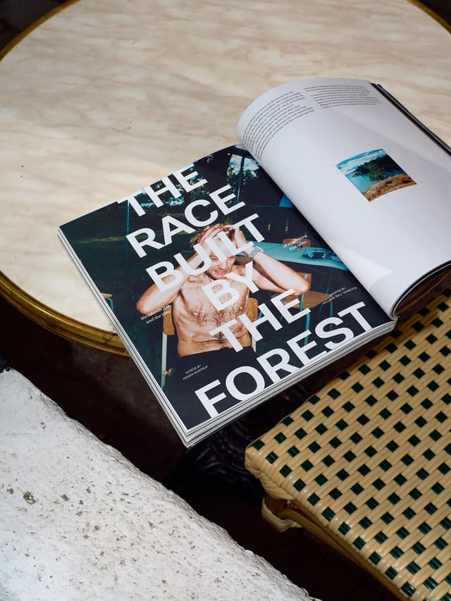 An open magazine titled "THE RACE BUILT BY THE FOREST" with a shirtless man on its cover rests on a marble table.