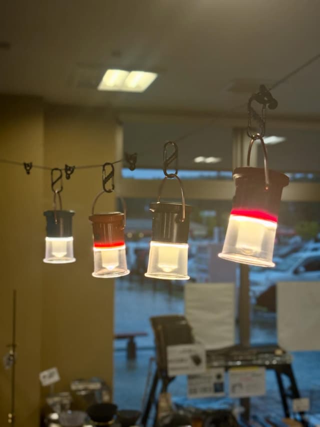 Four small, lit lanterns hang in a row, one glowing red and white, and another having a red band.