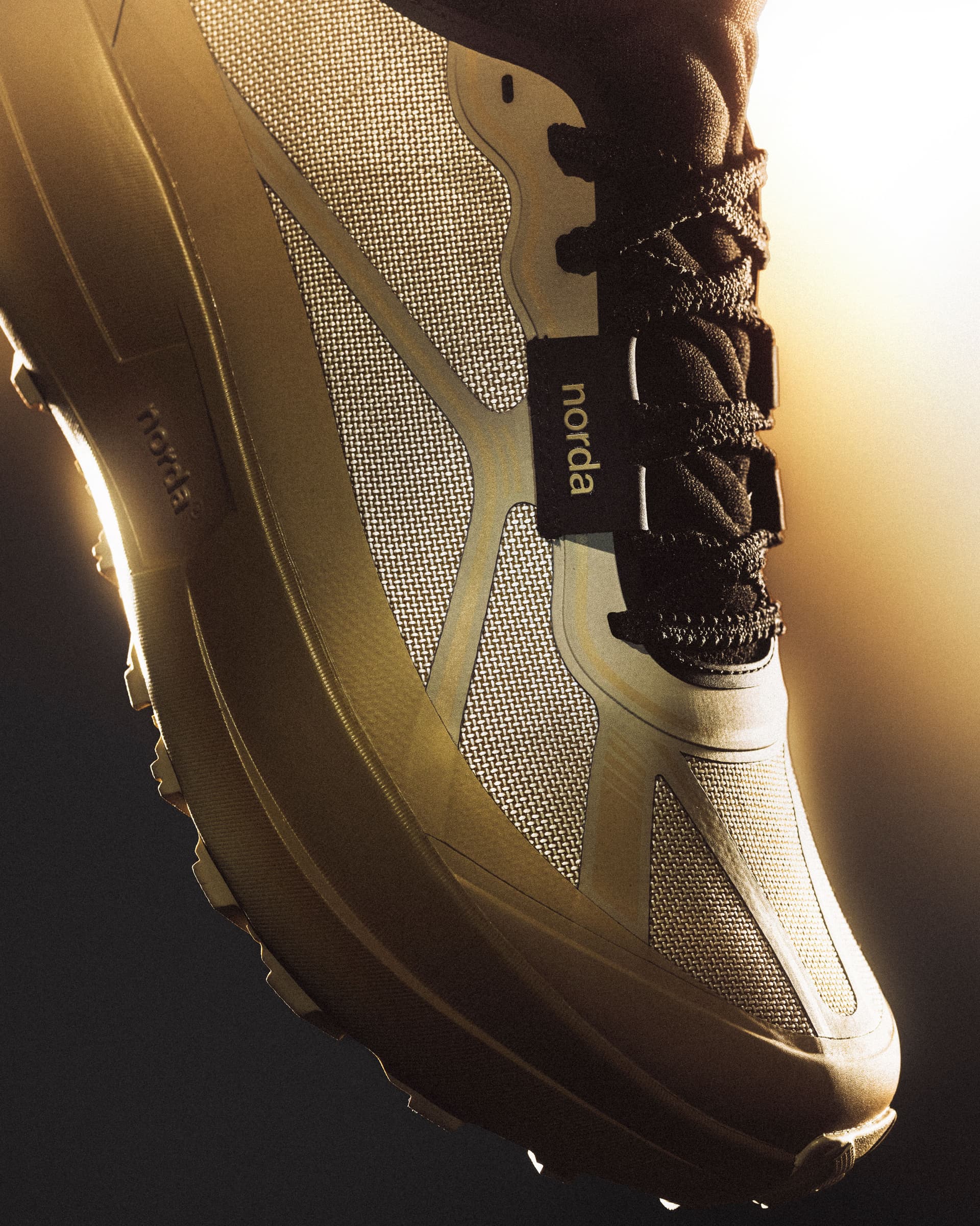 Close-up of a golden-brown Norda trail running shoe with a mesh upper and dark laces.