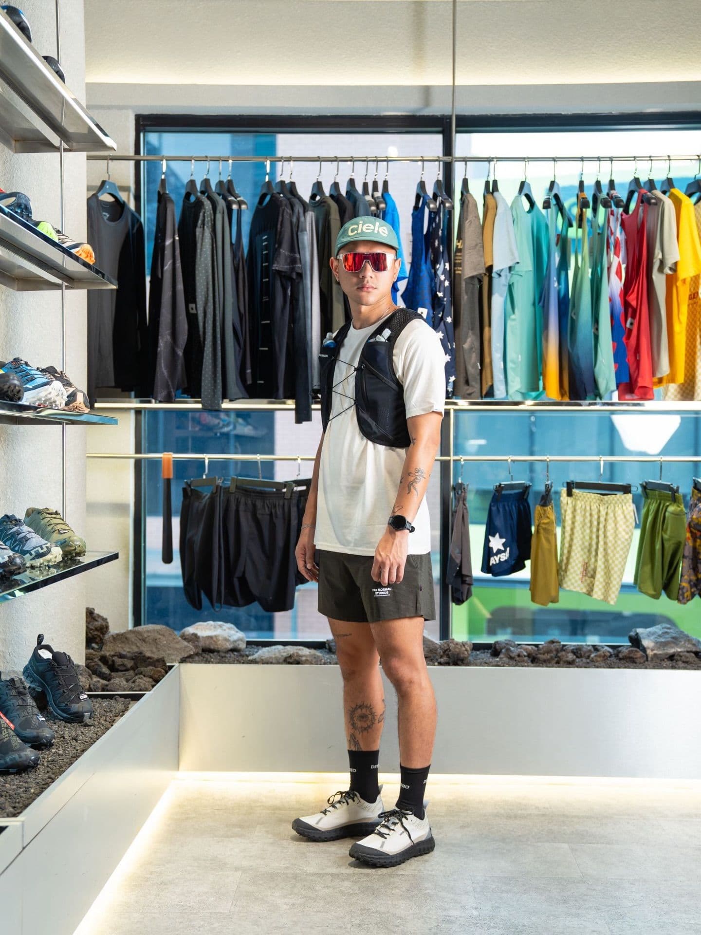 A person wearing a mint green cap, red sunglasses, and a running vest poses in a sportswear store.