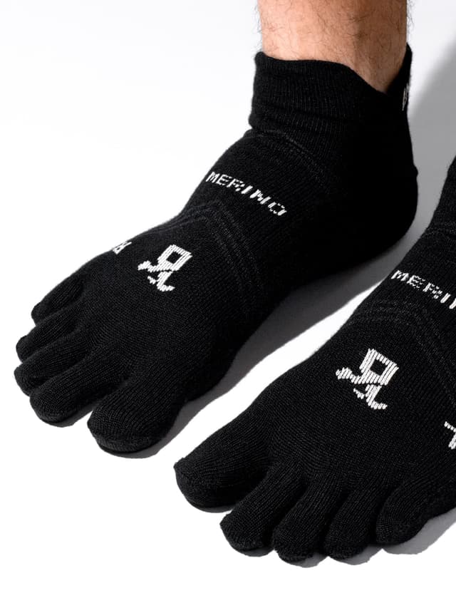 Black Merino five-toe socks with a white logo worn on feet.