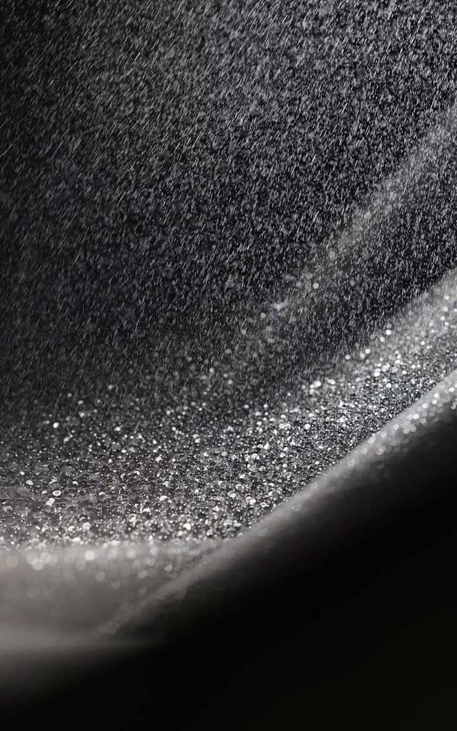Silver droplets raining onto and collecting on a dark, curved surface.