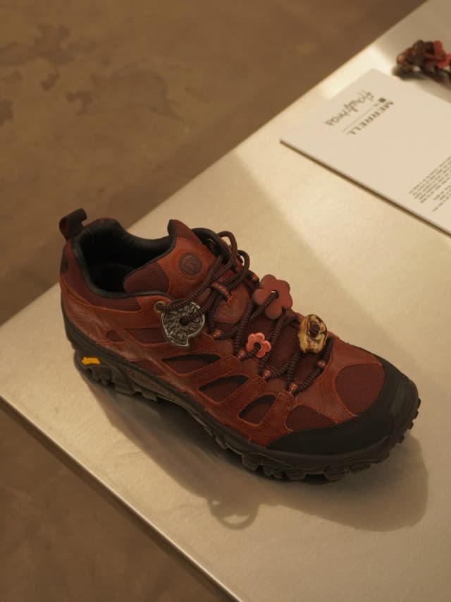 A reddish-brown hiking shoe with flower-shaped charms on its laces.