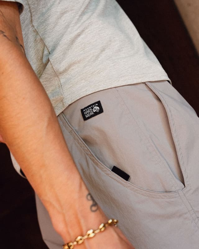 Person in light grey shirt and Mountain Hardwear pants, with a gold bracelet on their arm.