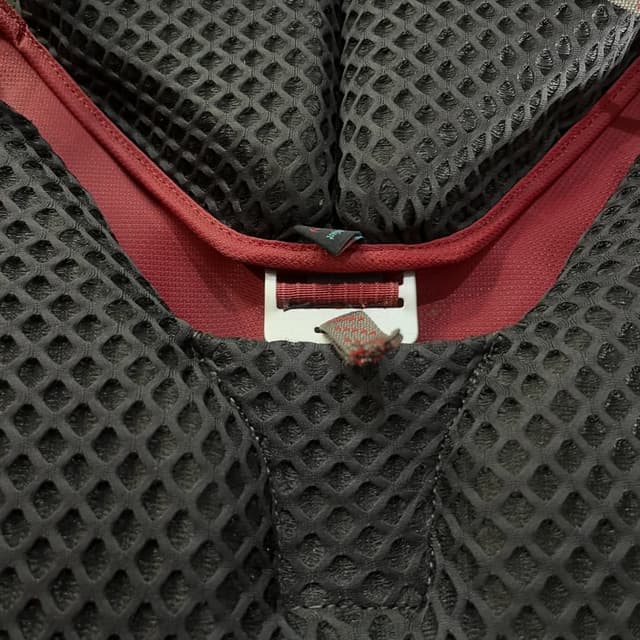 Dark mesh fabric with red trim and a white strap adjuster.