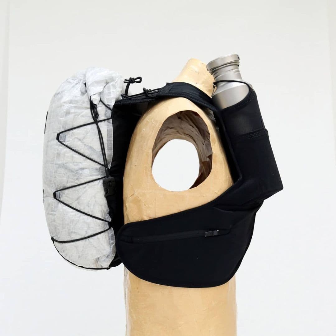 Black chest pack with a white crinkled pouch and a silver water bottle, modeled on a mannequin.