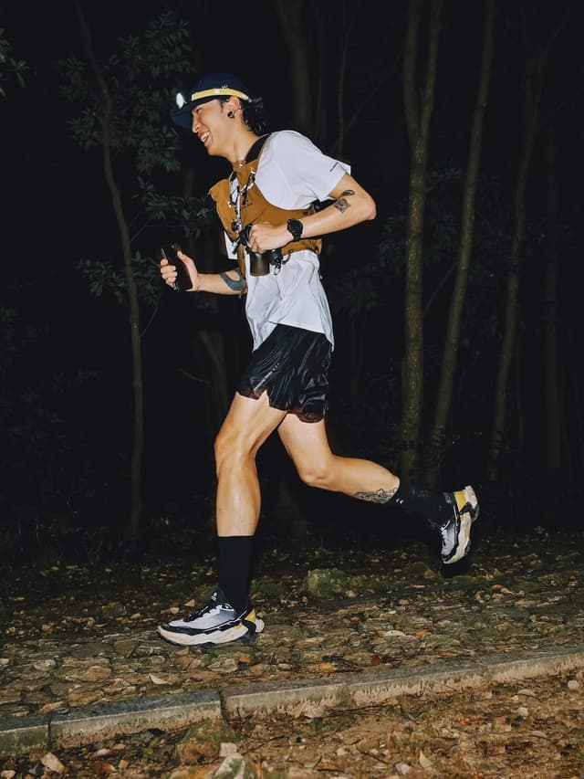 A smiling person trail running at night, illuminated by a headlamp.