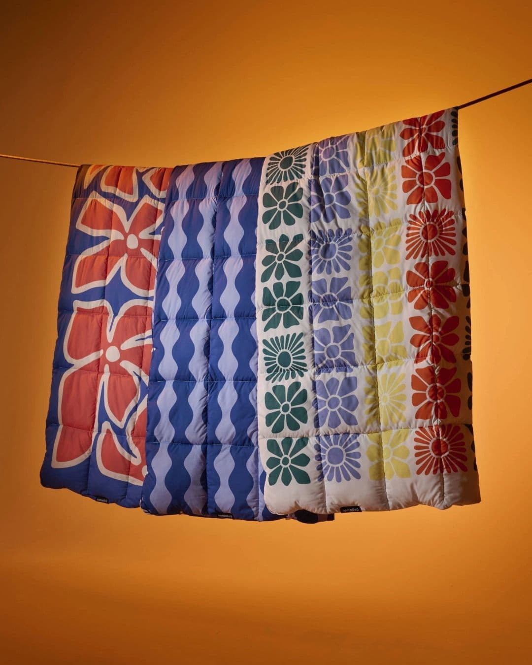 A colorful quilted blanket with floral and wavy patterns hanging against an orange background.