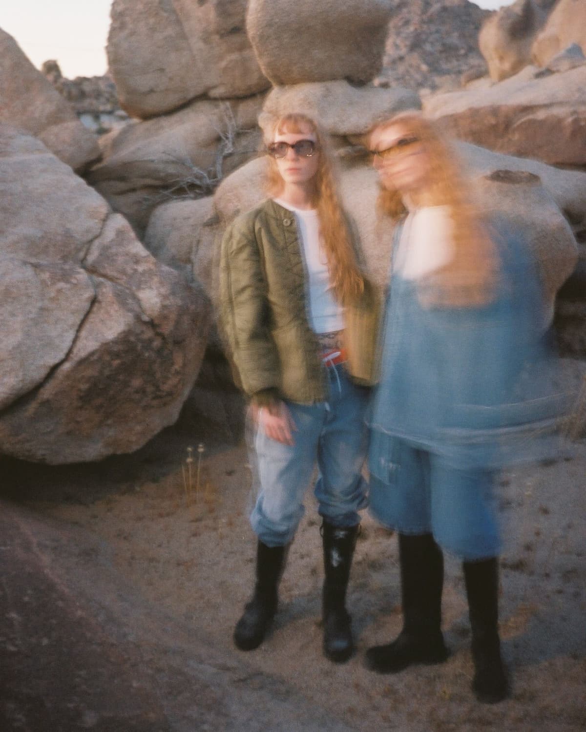 Motion-blurred photo of two women in a rocky desert, one clearly visible in a green jacket and sunglasses.